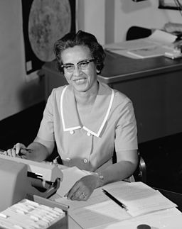 BLack and white photo of Katherine Johnson sitting at her desk, smiling